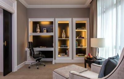 Office with a chair and ottoman in one corner, a built-in desk and bookcases on the opposite wall and plenty of natural light
