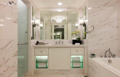 Shower and tub separated by a vanity with a single sink, all awash in white marble with grey veining