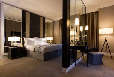 Suite bedroom in gray with tall ceilings, mirrored wall panels and a floating wall separating it from the sitting area