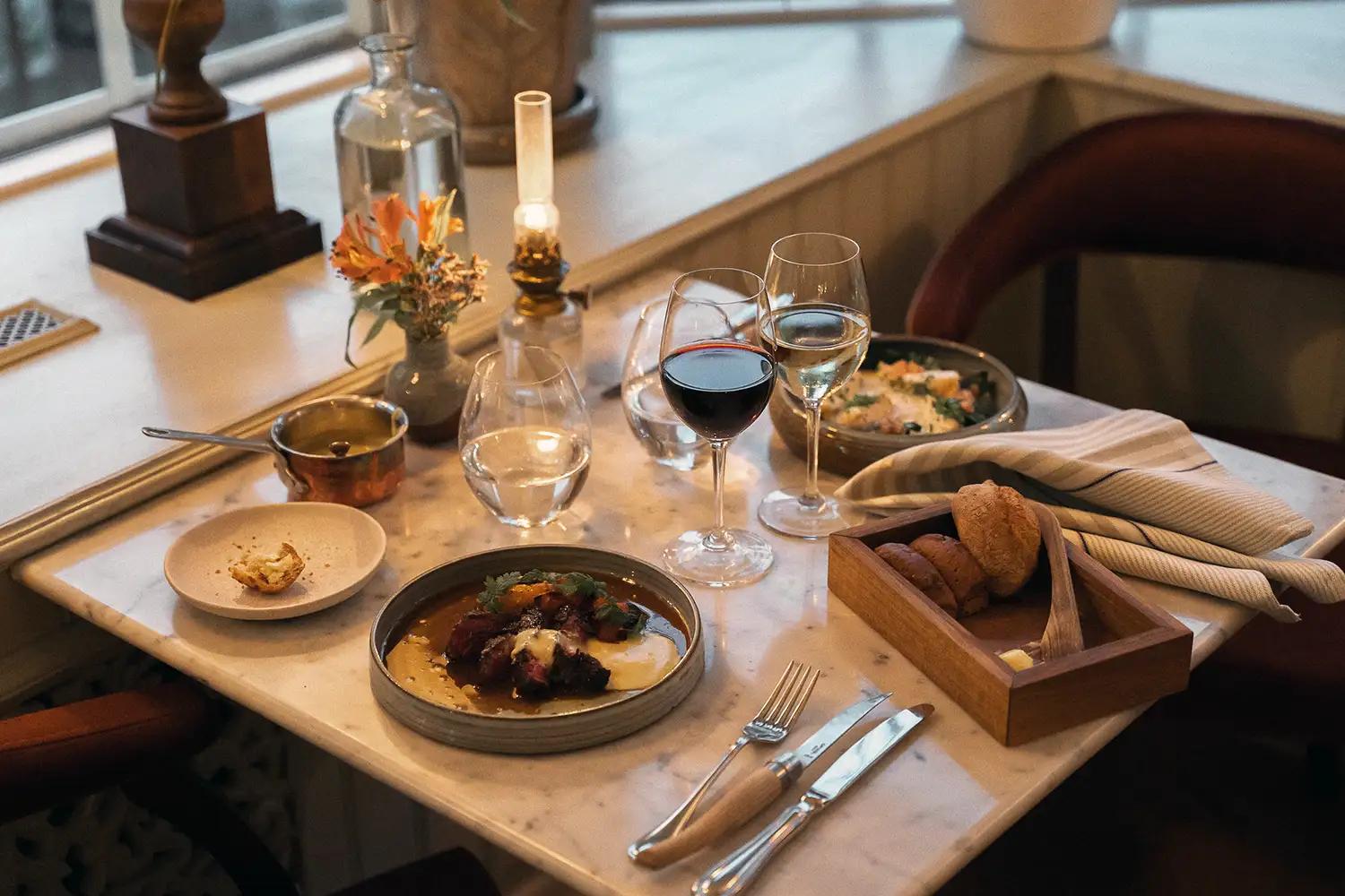 Elegant dukat bord med varmrätt, bröd, vin och stämningsfull belysning i restaurangmiljö på Ystad Saltsjöbad.