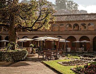 A large cedar tree hangs over tables and chairs, shaded from sun by wide cantilever parasols, in the picturesque courtyard.