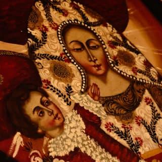 A detail of an 'Our Lady of the Rosary' painting of the Virgin Mary with an infant Jesus, in rich gold, red and cream tones.