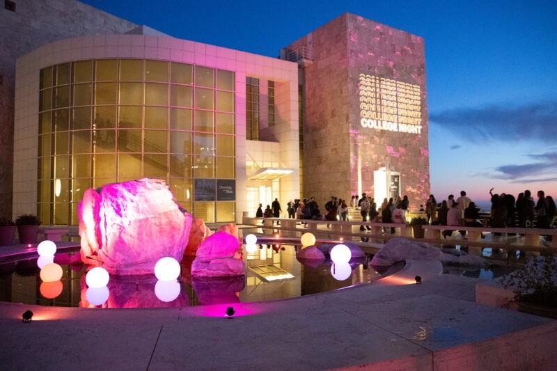 People wander through the courtyard of a large, modern building, taking photos and laughing.