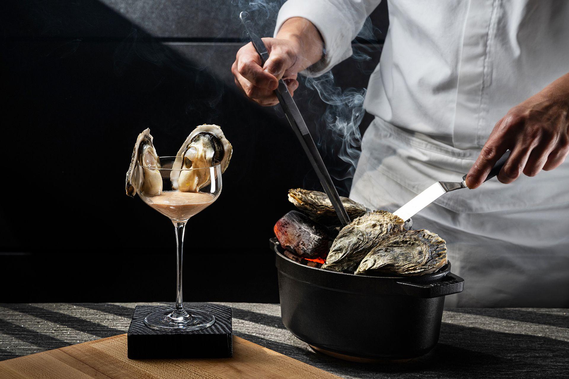 At Grill58, the seasonal oysters are presented through an engaging tableside approach. Two freshly shucked oysters are perched on a stemmed glass over a light dressing, enhanced by a subtle smoke effect that adds depth to the aroma. Behind them, a cast‑iron pot filled with steaming shells highlights the freshness and quality of the seafood. This presentation reflects the restaurant’s modern steakhouse sensibility and offers a refined, flavour‑forward start to the meal.