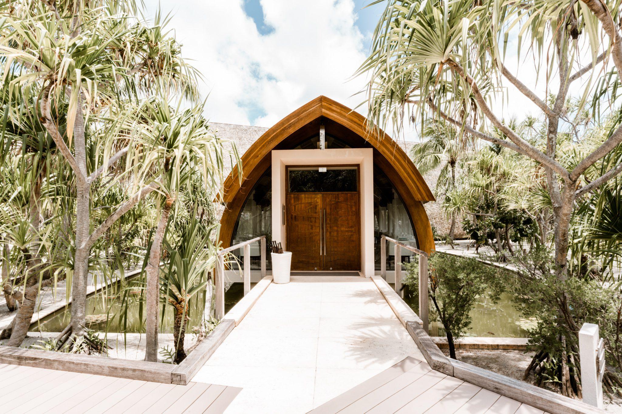 Wooden walkway surrounded by palms, leading to large double doors at the entrance of our Tahiti spa