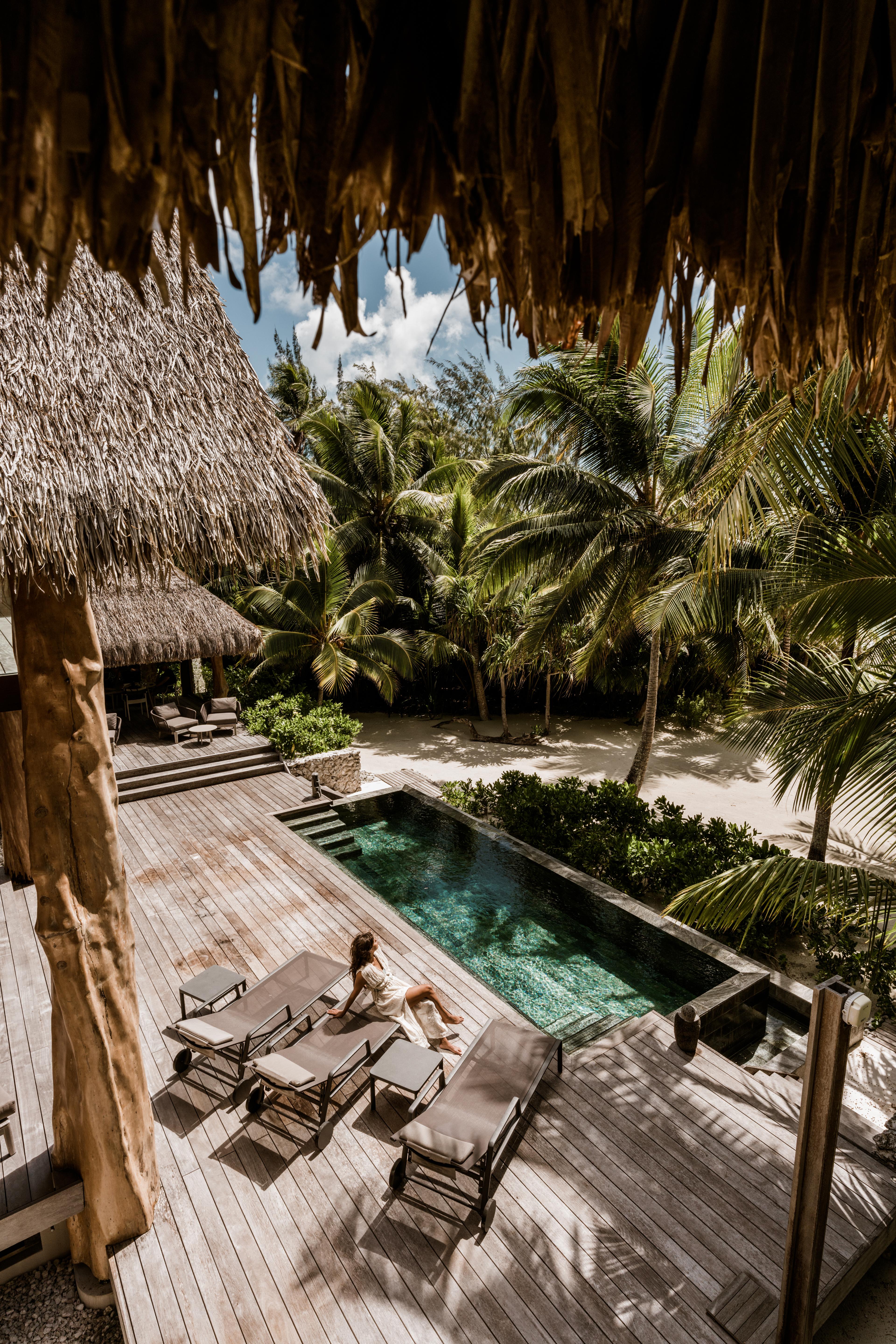 Woman relaxing on a pool deck among tropical trees at our Tahiti resort
