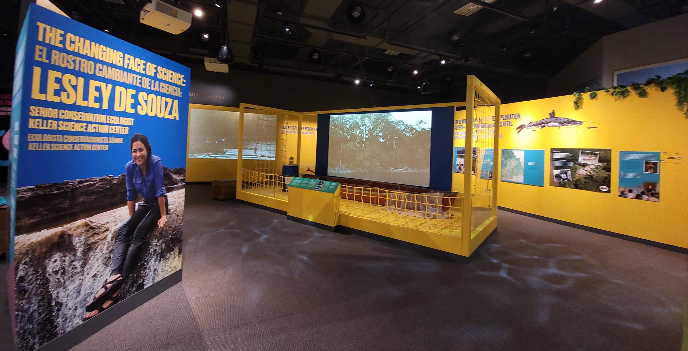 A museum exhibition space with large video screens and graphic panels.