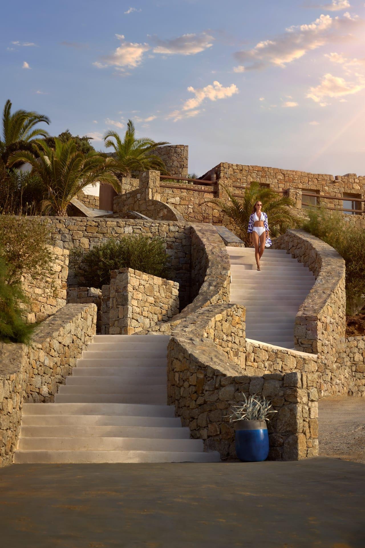 A lady stepping down the stairs by the stone walls at the Mykonos Grand hotel.